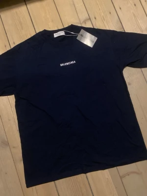 2021 balenciaga t-shirt - Snygg mörkblå t-shirt från Balenciaga med vit logga tryckt på både bröstet och ryggen. Klassisk passform och rund halsringning, perfekt för en stilren och trendig look.