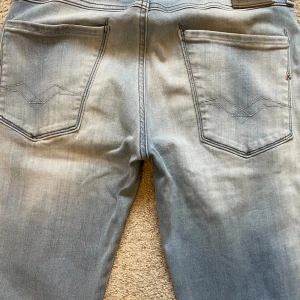 Replay Anbass Jeans - Snygga ljusblå jeans från Replay i modellen Anbass. De har en klassisk femficksdesign med knapp och dragkedja framtill. Perfekta för en avslappnad stil.                                                               Storlek: W28 L32