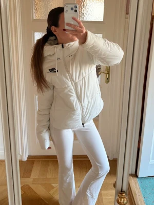Vit pufferjacka från Nike - Säljer en snygg vit pufferjacka från Nike med dragkedja och huva. Jackan har en stilren design med svart Nike-logga på bröstet och dragsko i huvan. Perfekt för kalla dagar när du vill hålla dig varm och se trendig ut. Köpt för runt 1000 kr 