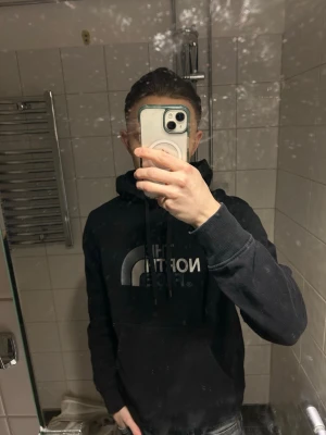 Svart hoodie från The North Face - Snygg svart hoodie från The North Face med stor logga i vitt och grått på bröstet. Klassisk modell med huva och dragsnören samt en stor magficka. Perfekt för en avslappnad och trendig stil. Villig att gå ner lite i pris för snabb affär!