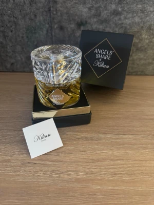 Angels' Share parfym från Kilian - Lyxig parfym från Kilian, Angels' Share, i en elegant glasflaska med kristalliknande lock och guldfärgad vätska. Flaskan har ett unikt mönster och levereras i en svart och guld ask. Perfekt för dig som gillar exklusiva dofter och snygg design.