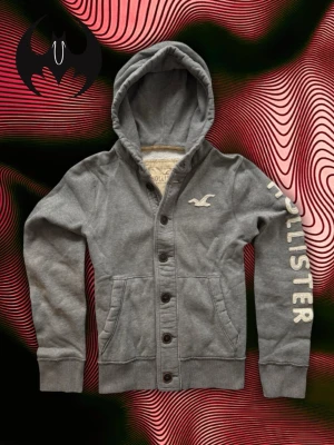 Grå Hollister Kofta (sällsynt) - Sällsynt Grå Hollister Kofta | mycket bra skick, snöre saknas | Size M/L | Längd: 68cm Axelbredd: 48cm Armlängd: 72cm | Modell, 178cm 60kg | Lägg endast bud med avsikt att köpa, inga fördröjning!