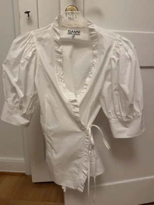 Vit omlottblus från Ganni - Snygg vit omlottblus från Ganni med puffiga korta ärmar. Använd endast en gång!!💕💕