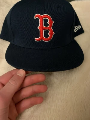 Mörkblå Boston Red Sox keps New Era - Säljer en mörkblå New Era 59FIFTY keps med Boston Red Sox logga i rött och vitt framtill. Klassisk rak skärm och broderad New Era-logga på sidan. Tillverkad i slitstarkt tyg, perfekt för dig som gillar sportig streetstyle.