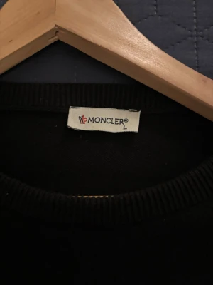 Svart Moncler tröja med logga - Snygg svart tröja från Moncler med rund halsringning och klassisk Moncler-logga på bröstet. Tröjan har ribbade muddar vid halsen och är tillverkad i ett mjukt material som känns skönt mot huden.