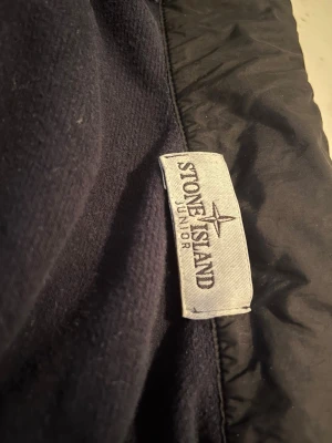 Mörkblå hoodie från Stone Island Junior - Snygg mörkblå hoodie från Stone Island Junior med klassisk logotyp på etiketten. Tillverkad i mjukt material som känns skönt mot huden. Perfekt för dig som vill ha en stilren och bekväm hoodie med streetwear-vibe.