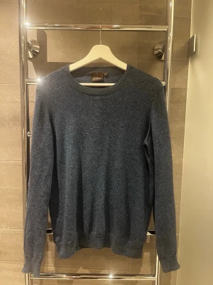 Mörkblå stickad tröja från Oscar Jacobson - Mörkblå stickad tröja från Oscar Jacobson med rund halsringning och ribbade muddar vid ärmslut och nederkant. Tröjan har en klassisk, enkel design och är tillverkad i mjukt material som passar perfekt till lager på lager. Nypris ca: 1000kr. Storlek S. Skriv vid frågor!