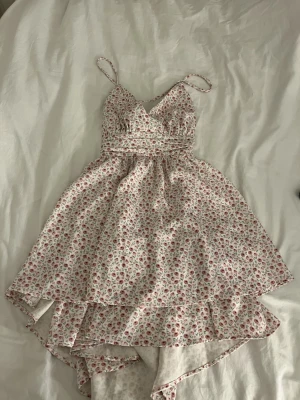 Blommig sommarklänning med volang - Söt kort blommig klänning med volangkant och smala axelband som korsas i ryggen . Klänningen är aldrig använd.