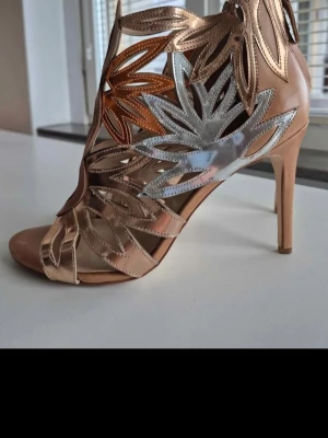 Metallic pumps med bladmönster - Unika pumps med öppen tå och klack, dekorerade med bladformade detaljer i guld, silver och kopparfärgat läder. Snyggt utskurna sidor och dragkedja bak. Perfekta för dig som vill sticka ut med en kreativ och trendig look.