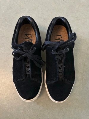  Nya Svarta mocka sneakers från EyTYS - Stilrena svarta sneakers från EYTYS med ovandel i mocka och klassiska svarta skosnören. Skorna har en vit sula som ger en snygg kontrast och en enkel, tidlös design. Perfekta för dig som gillar minimalistisk stil och vill ha ett par schyssta sneakers till vardags. Använda två gånger 