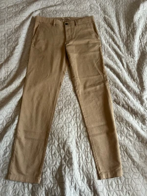 Beige chinos  - Använda 2 gånger. Snygga beige chinos med klassisk design. Byxorna har två sidofickor fram och två bakfickor med knapp. Tillverkade i ett mjukt och slitstarkt material som ger en clean look. Perfekta för dig som gillar stilrena och enkla plagg.