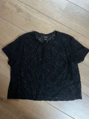 Svart spetsblus från Monki - Säljer en svart blus från Monki i genombruten spets med blommönster. Toppen har korta ärmar, rund halsringning och är croppad i modellen. Fråga gärna vid frågor 💕