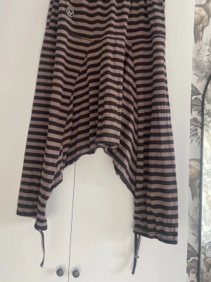 Randiga haremleggings med knytband - Unika leggings med svart och beigea ränder i haremstil. De har låg gren, vida ben och knytband vid bensluten. Perfekta för dig som gillar en avslappnad och cool look. Mjukt och stretchigt material.