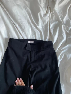 Svarta kostymbyxor från Nelly - Snygga svarta kostymbyxor från Nelly med klassisk rak passform och hög midja. Byxorna har hysk- och hakstängning samt diskret dragkedja. Perfekta för en stilren look och lätta att matcha med olika toppar.