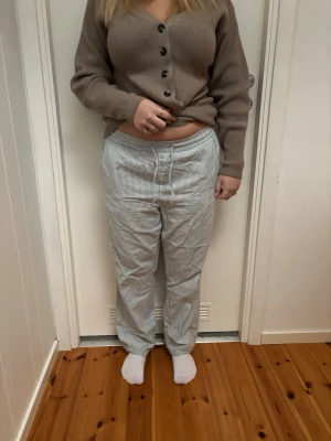 Randiga pyjamasbyxor i bomull - Säljer ett par klassiska pyjamasbyxor med tunna blå och vita ränder. Byxorna har rak passform, resår i midjan och knytband framtill för extra komfort. Tillverkade i mjuk bomull som känns skön mot huden, perfekta för slappa dagar hemma.