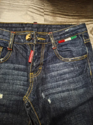Mörkblå jeans från D - Snygga mörkblå jeans från D med slitna detaljer och kontrasterande gula sömmar. Klassisk femficksmodell med röd D-tag och broderad detalj i italienska flaggans färger vid fickan. Raka ben och låg midja, perfekt för en avslappnad stil. Bästa är att få mått för otydlig storlek 👍