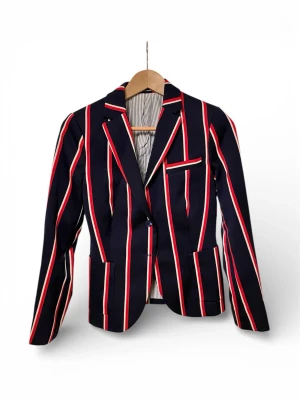 Marinblå kavaj med röda ränder - Snygg marinblå kavaj med vertikala röda och vita ränder. Klassisk modell med två knappar framtill, tre fickor och smal passform. Fodrad insida med randigt tyg. Perfekt för en trendig och ungdomlig stil.
