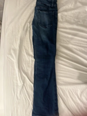 Mörkblåa utsvängda jeans storlek:152 - Snygga mörkblå jeans med raka ben och markerade sömmar. Jeansen har stora fyrkantiga fickor fram och dubbla metallknappar i midjan. Klassisk tvättad denim-look som passar till det mesta. Perfekta för dig som gillar en enkel men trendig stil.