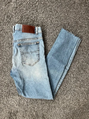 Ljusblå jeans från Tiger of Sweden - Säljer ett par ljusblå  jeans från Tiger of Sweden. Jeansen har klassisk femficksdesign, läderpatch bak i midjan och är tillverkade i stretchig denim för en bekväm passform. Perfekta för en avslappnad och trendig look. Avklippta så är som längd 30