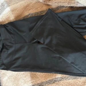 Svarta bootcut träningsbyxor med hög midja - Säljer ett par svarta bootcut träningsbyxor med hög midja och tight passform. De är stretchiga och mjuka, perfekta för en avslappnad look. Materialet känns lent och följsamt mot huden. Inga synliga loggor eller detaljer.