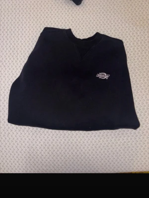 Svart sweatshirt från Dickies - Klassisk svart sweatshirt från Dickies med rund halsringning och ribbade muddar. Diskret Dickies-logga broderad på bröstet. Perfekt basic-plagg för en avslappnad streetwear-look.