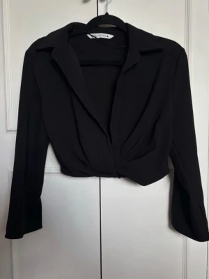 Svart croppad zara blus - Stilren svart croppad omlottopp från Zara med slits vid ärmarna. Toppen har en twistad omlottdesign framtill. Använd mycket få gånger nästintill som ny. 