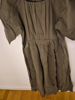Olivgrön klänning från Mango - Olivgrön klänning från Mango med lös passform och kort ärm. Klänningen har rund halsringning och resår i midjan för en avslappnad siluett. Tillverkad i ett mjukt bomullstyg som känns skönt mot huden.