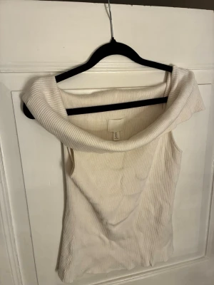 Vit ribbad offshoulder topp H&M - Säljer en vit ribbad offshoulder topp från H&M. Toppen har en bred, vikt krage som ger en snygg och trendig look. Perfekt att styla med jeans eller kjol för en clean och fräsch outfit.
