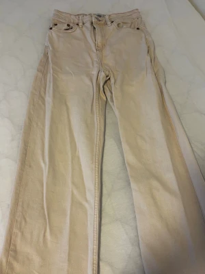 Beige raka jeans från lager 157 - Säljer ett par beige jeans från lager 157 med rak passform och klassisk femficksdesign. Jeansen har hög midja och är tillverkade i ett kraftigt bomullstyg. Perfekta för en clean och avslappnad stil.
