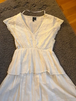 Vit sommarklänning med spetsdetaljer - Söt vit klänning från H&M med v-ringning och spetsdetaljer på överdelen. Klänningen har volang vid midjan och är ärmlös med breda axelband. Perfekt för varma dagar och har en luftig, romantisk känsla.