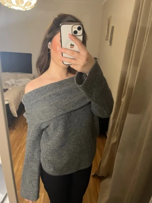 Grå off-shoulder stickad tröja - Säljer en snygg grå stickad tröja med off-shoulder design och bred krage. Tröjan har långa ärmar och är gjord i ett mjukt stickat material som känns skönt mot huden. Perfekt för dig som vill ha en trendig och bekväm look.
