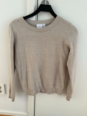 Beige stickad tröja från Vila - En enkel och stilren beige stickad tröja från Vila med rund halsringning och ribbade muddar vid ärmslut och nederkant. Perfekt basplagg att matcha till olika outfits.