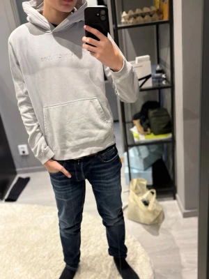 Ljusgrå hoodie från Calvin Klein Jeans - Snygg ljusgrå hoodie från Calvin Klein Jeans med broderad logga på bröstet. Klassisk känguruficka framtill och ribbade muddar vid ärmar och nederkant. Tillverkad i mjukt bomullsmaterial och har en stor huva för extra komfort.