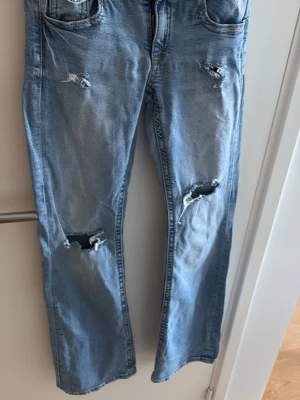 Ljusblå slitna jeans med hål - Ljusblå jeans med raka ben och flera slitningar samt hål på båda knäna och låret. Klassisk femficksmodell med dragkedja och knapp. Perfekta för en avslappnad och trendig stil. Från Gina Young men har gjort hål själv.