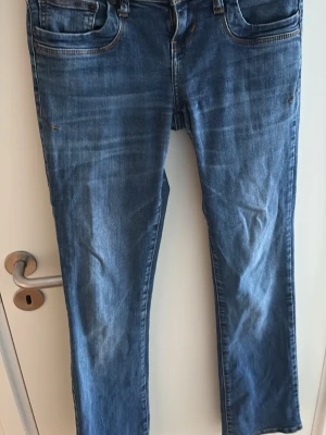 Blå bootcut jeans med slitningar - Ett par klassiska blå jeans med diskreta slitningar. Jeansen har fem fickor och låg midja. Perfekta för en avslappnad och trendig look. Stl W25 L32