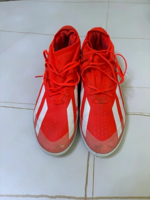 Röda Adidas futsal fotbollsskor med vita ränder - Säljer ett par röda Adidas fotbollsskor med klassiska vita ränder på sidorna. Skorna har snörning, högre skaft och är tillverkade i syntetmaterial för bra passform och kontroll på planen. Röda Adidas fotbollsskor med vita ränder för dig som vill sticka ut på fotbollsplanen.