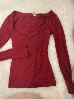 Vinröd långärmad topp från Nelly - Snygg vinröd långärmad topp från Nelly med v-ringning och spetsdetalj längs halsringningen. Modellen är figurnära och har en enkel.