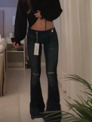 Mörkblå bootcut jeans med låg midja - Säljer ett par mörkblå bootcut jeans med låg midja och vita kontrastsömmar. Jeansen har utsvängda ben, dekorativa sömmar och knappdetalj i midjan. Perfekta för en trendig och avslappnad look. Ifrån Gina ❣️