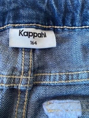 Blå bootcut jeans från Kappahl - Säljer ett par blå bootcut jeans från Kappahl i storlek 164. Jeansen har klassisk femficksdesign med ficklock bak och kontrastsömmar. Tillverkade i mjukt denimtyg som ger en skön passform och retrovibe.