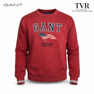 Gant New Haven Crewneck Sweatshirt - GANT New Haven Crewneck Sweatshirt – Red  A deep red GANT crewneck sweatshirt with a softly worn character and timeless collegiate spirit. The bold embroidered GANT lettering arches above an American flag motif, finished with “New Haven Conn. USA” beneath. Ribbed cuffs and hem frame its classic silhouette. A piece that carries heritage in every thread and feels effortlessly grounded the moment you slip it on.  Please feel free to reach out with any questions.