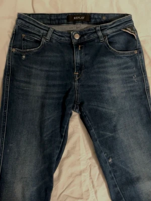 Mörkblå jeans från Replay - Snygga mörkblå jeans från Replay med klassisk femficksdesign och diskreta slitningar. Jeansen har raka ben och är tillverkade i ett mjukt denimtyg som ger en skön passform. Perfekta för dig som gillar en tidlös och avslappnad stil.