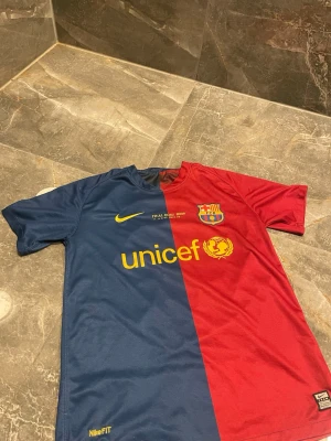 Barcelona matchtröja Nike blå/röd - Säljer en klassisk FC Barcelona matchtröja från Nike med halva tröjan i blått och halva i rött. Tryck med Unicef och klubbmärke på bröstet samt Nike-logga. Tillverkad i lätt och ventilerande material, perfekt för fotboll eller träning.