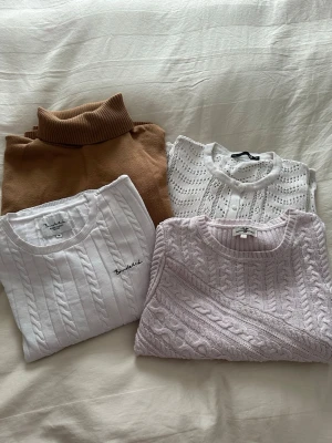 Stickade tröjor i neutrala toner - Fyra stickade tröjor i olika stilar och färger: en brun polotröja, en vit kabelstickad tröja från bondleid, en vit hålstickad kofta från lager 157, och en ljuslila kabelstickad tröja från Support Republic. Perfekta för lager på lager och mysiga dagar.
