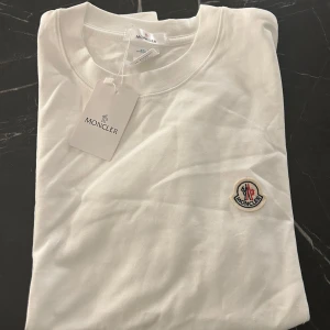 Vit Moncler t-shirt strl m -  Moncler Tshirt Strl M Vit, aldrig använd inga slitage eller liknande. Väldigt fin och fräsch!   Finns i Stockholm, kan mötas upp samt fraktas!