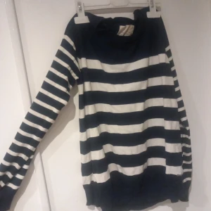 Randig marinblå och vit tröja - Säljer en långärmad tröja med breda marinblå och vita ränder. Tröjan har en avslappnad passform, rund halsringning och ribbade muddar vid ärmslut och nederkant. Perfekt för en casual look och enkel att matcha med jeans.