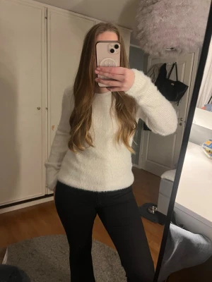 Vit fluffig stickad tröja - Säljer en vit stickad tröja med fluffig och mjuk känsla. Tröjan har rund hals och långa ärmar, perfekt för att hålla sig varm. Passar dig som gillar en enkel och stilren look.