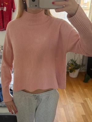 Ljusrosa stickad tröja med polokrage - Mysig ljusrosa stickad tröja med hög polokrage och ribbade detaljer vid hals, ärmslut och nederkant. Tröjan har en boxy passform och är tillverkad i ett mjukt, fluffigt material som känns skönt mot huden. Perfekt för kyliga dagar. Den är alltså inte nopprig, utan den är stickad så som visas på bild 2. Märkt som M men mer en S. 