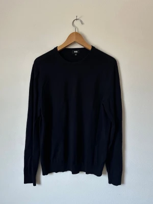 Mörkblå stickad tröja från Uniqlo - En stilren mörkblå stickad tröja från Uniqlo med rund halsringning och långa ärmar. Tröjan har en enkel och klassisk design med ribbade muddar vid ärmslut och nederkant. Perfekt basplagg för lager på lager och passar till det mesta. 8D5