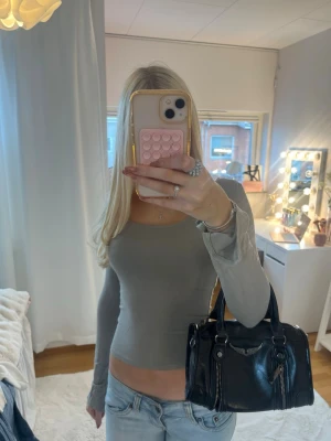 Grå tight långärmad topp - Säljer en grå, tight långärmad topp med rund halsringning. Toppen är croppad och har en enkel, stilren design som passar perfekt till jeans eller kjol. Materialet ser mjukt och stretchigt ut för en bekväm passform.