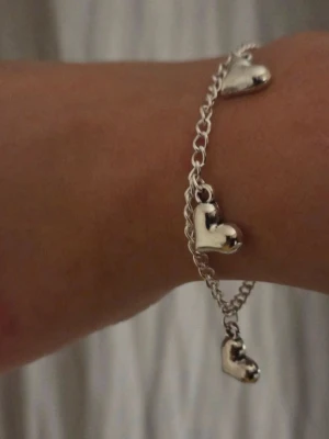 Silverfärgat armband med hjärtberlocker Rostfritt Stål  - Snyggt handgjort armband i silverfärgat rostfritt stål med tre hjärtformade berlocker. Kedjan är tunn och har ett klassiskt karbinlås. Perfekt för dig som gillar enkla men söta detaljer till din stil.